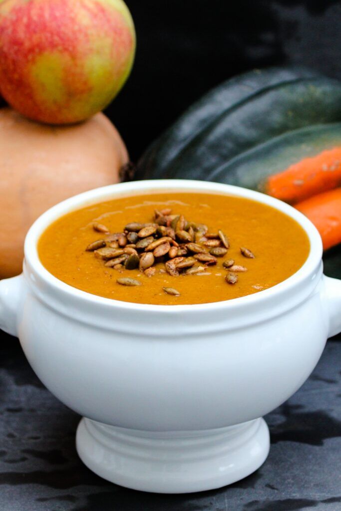 a white bowl filled with carrot soup next to some squash and pumpkins on a table