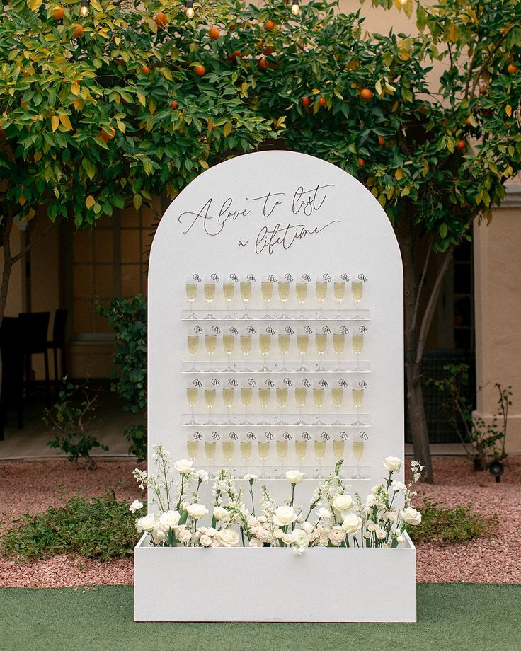 a white sign with wine glasses and flowers on it in front of an orange tree