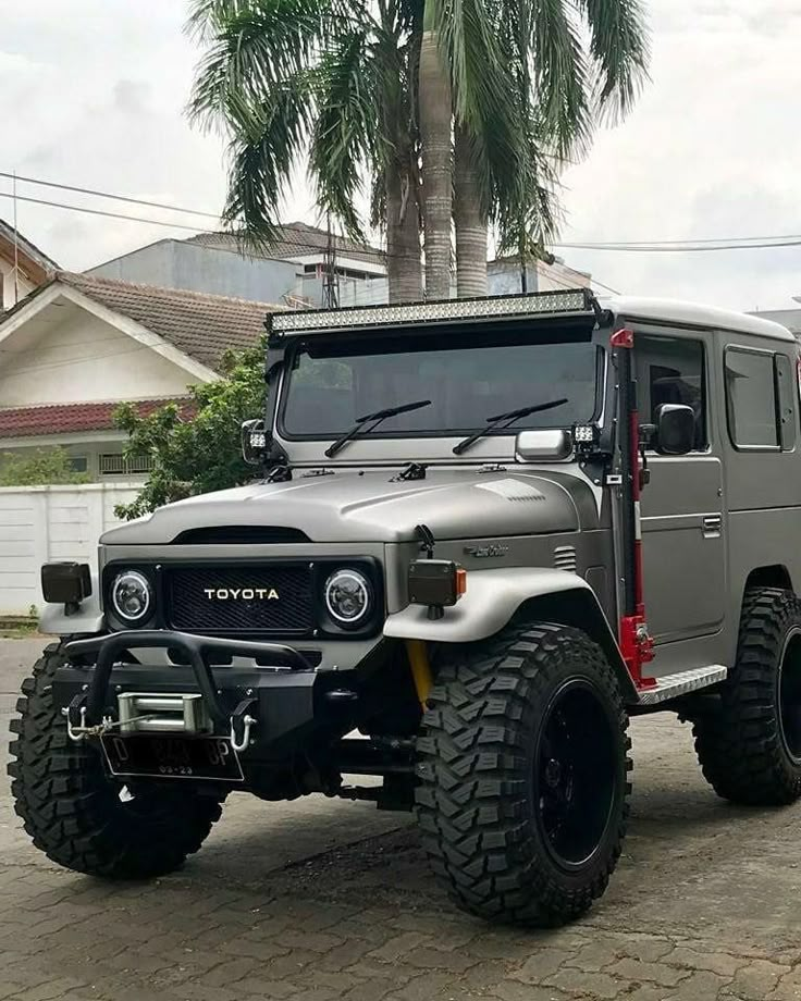 a large gray truck parked on top of a street next to a palm tree in front of a house