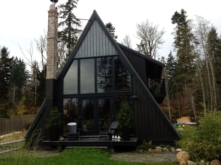 a large black house sitting on top of a lush green field next to a forest