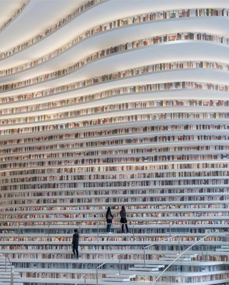 two people are standing in front of a large stack of books on the wall,