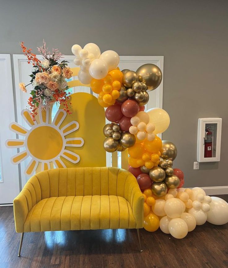 a yellow chair with balloons attached to it in front of a sun shaped balloon arch