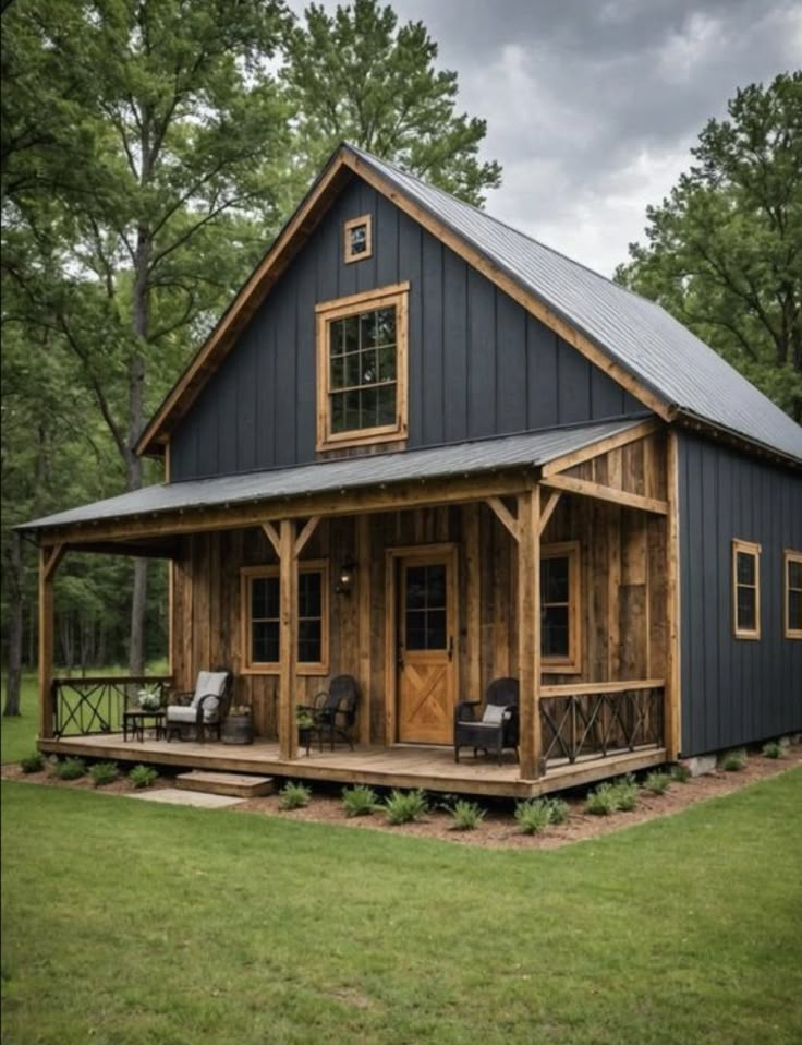 a small house with a porch and covered in wood, surrounded by green grass and trees