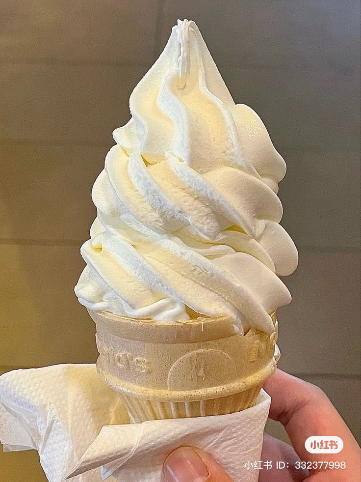 a hand holding an ice cream cone with white frosting on it's wrapper