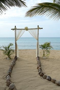 an outdoor wedding set up on the beach with white drapes and stone walkway leading to the ocean