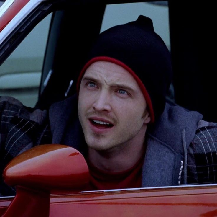 a man in a red car wearing a black beanie and looking out the window