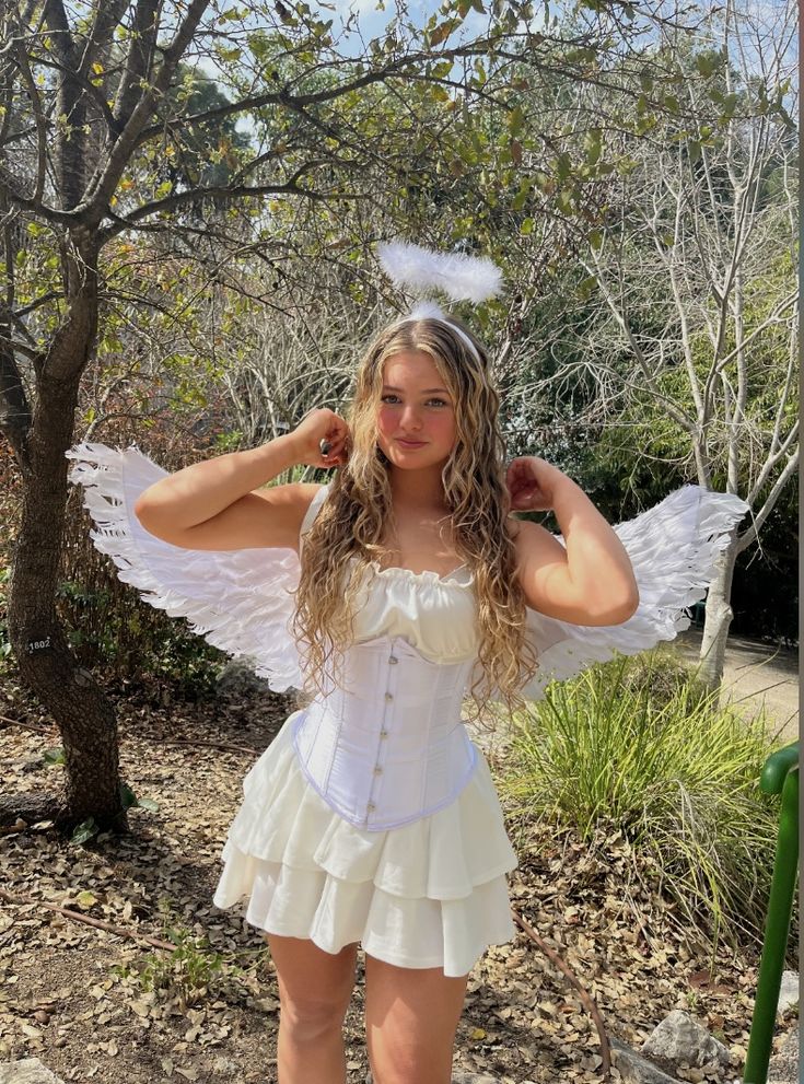 a woman in a white corset and angel wings poses for the camera with her hands behind her head