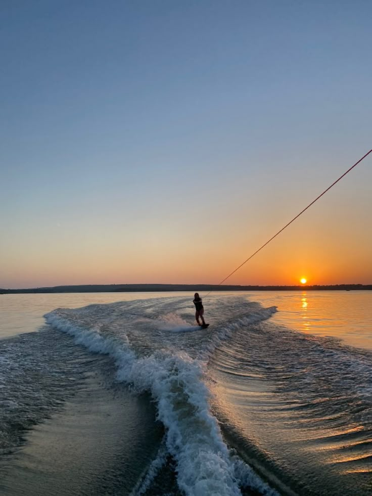 a person riding a wake board on top of a body of water at sunset with the sun in the distance