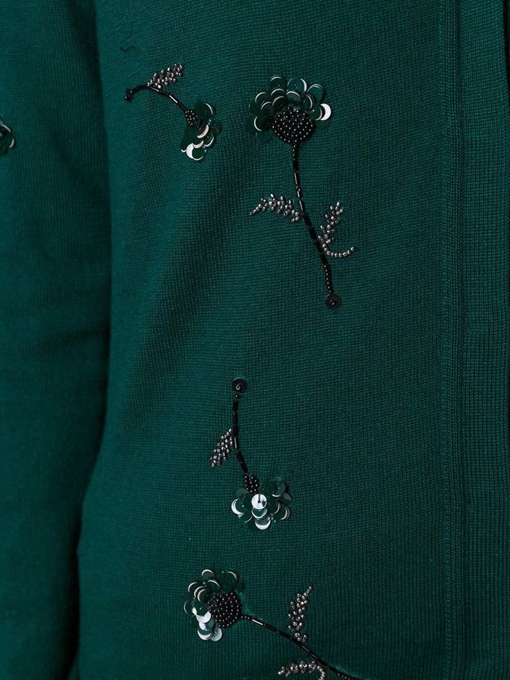 a person wearing a green sweater with embroidered flowers on the front and side, close up