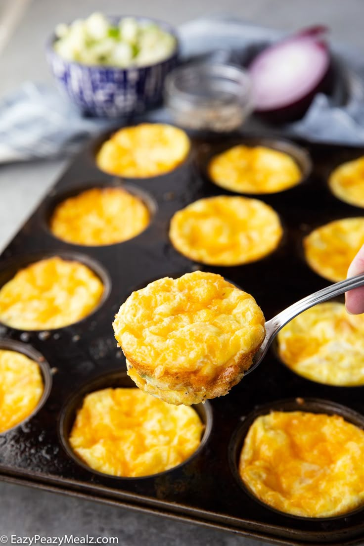 a person holding a spoon over a muffin tin filled with eggs and other food