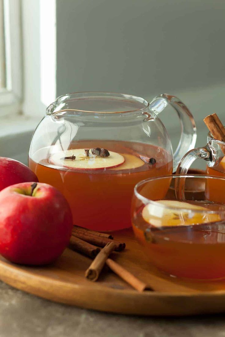 two glasses of apple cider on a tray with cinnamon sticks and apples in the background