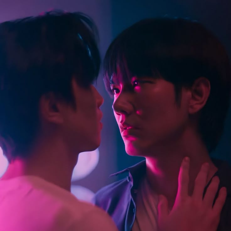 two young men standing next to each other in front of a pink light with their hands on their chest