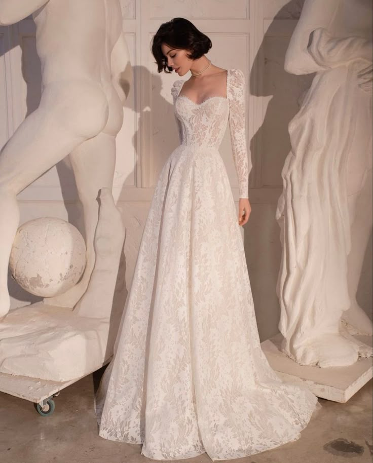 a woman standing in front of statues wearing a wedding dress with long sleeves and an open back