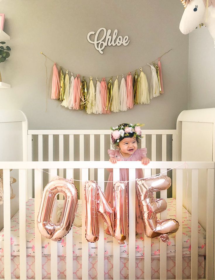 a baby in her crib with the word mom spelled out and balloons hanging from the ceiling