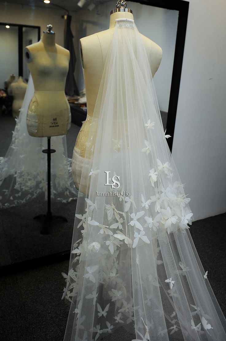 wedding veil with white flowers on display in front of mannequin's dummys