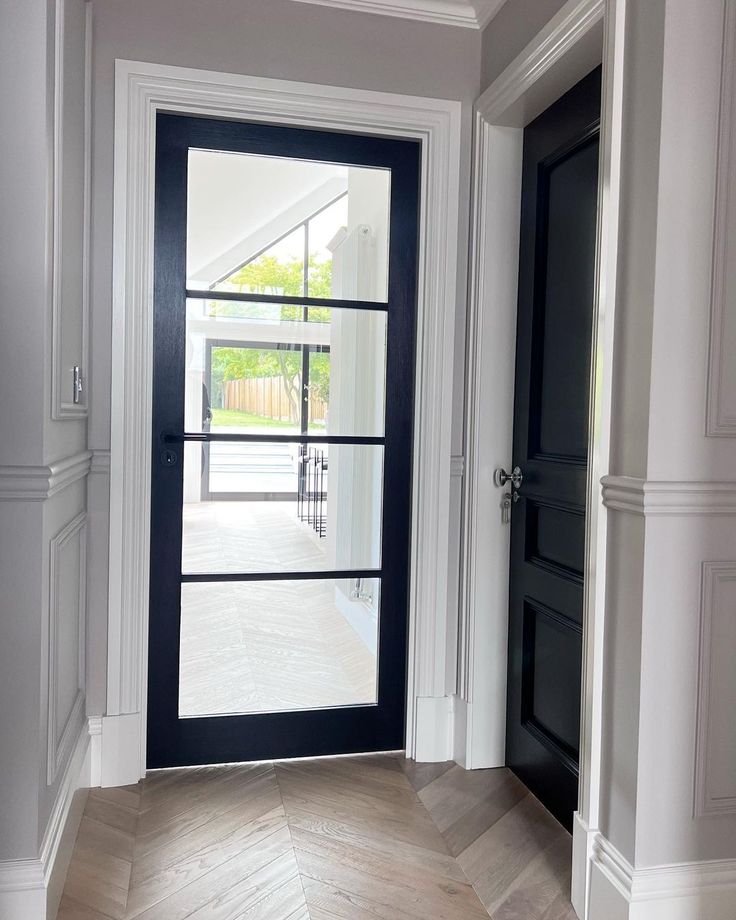 an empty hallway with two black doors and white trim on the walls, along with wooden flooring