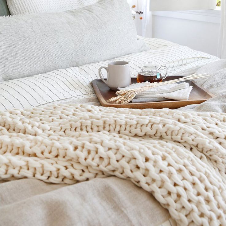 a tray with a coffee cup on top of a bed next to a white blanket