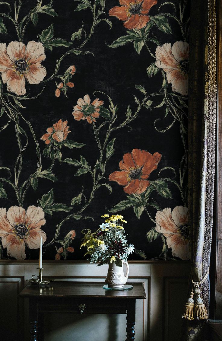 a vase with flowers on a table in front of a floral wallpapered wall