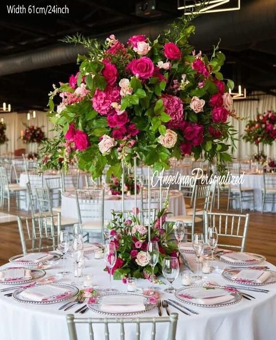 the table is set with pink and red flowers in tall vases on each side