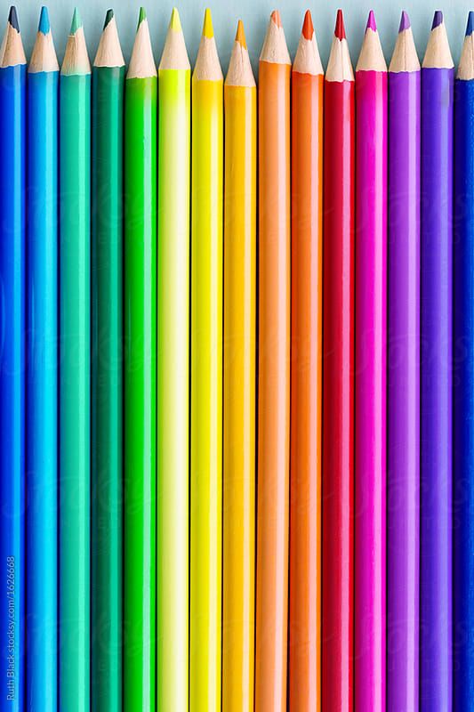 a row of colored pencils lined up against a white background with the top one in rainbow colors