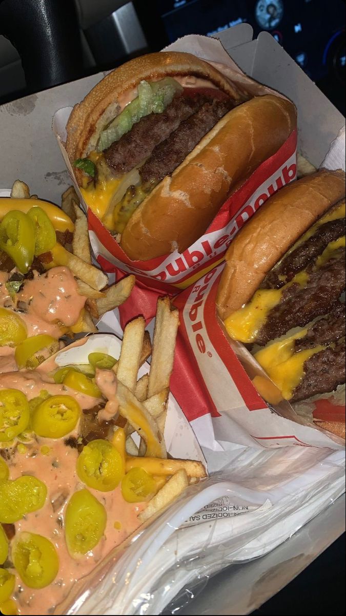 two cheeseburgers and fries are sitting in wrappers on the table next to each other