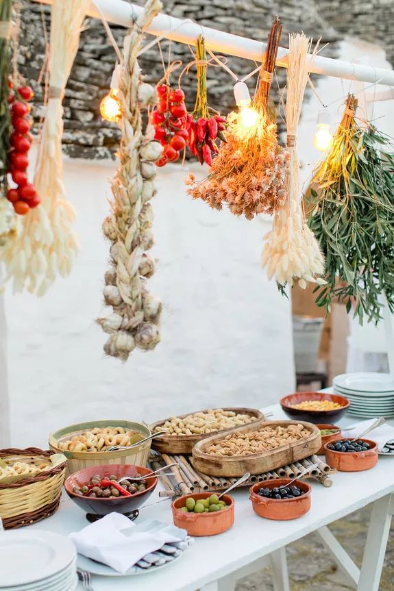 a table topped with lots of food next to a white wall covered in hanging lights