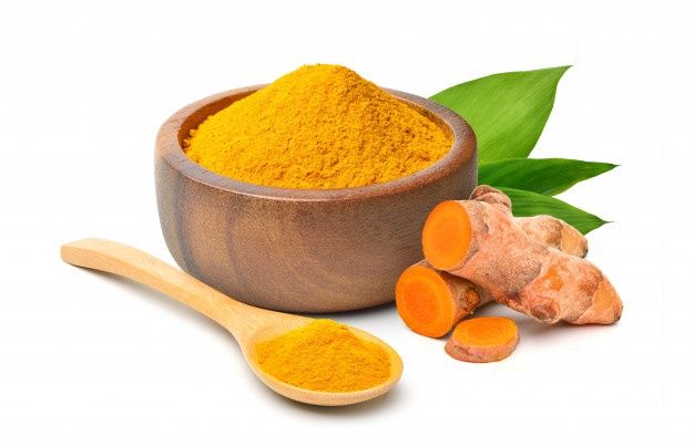 tumerical and ginger powder in a wooden bowl next to fresh tumerica leaves