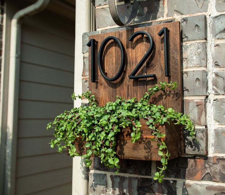 a house number sign on the side of a building with plants growing out of it