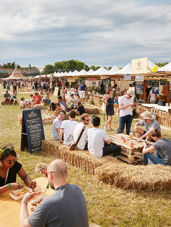 people sitting on hay bales eating food at an outdoor event with tents in the background