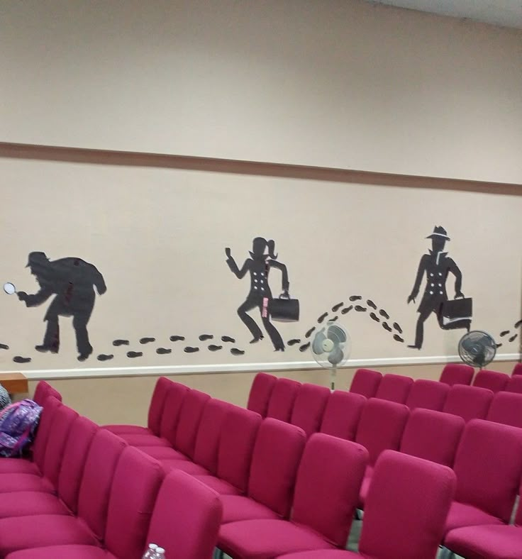 an empty room with pink chairs in front of a wall painted with black silhouettes