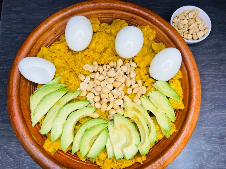 an assortment of food in a bowl with eggs, avocado and peanuts on the side