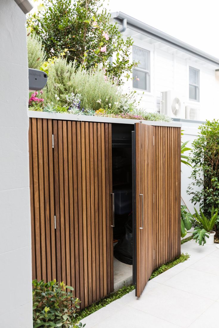 an outdoor storage shed with wooden slats on the sides and plants growing on top