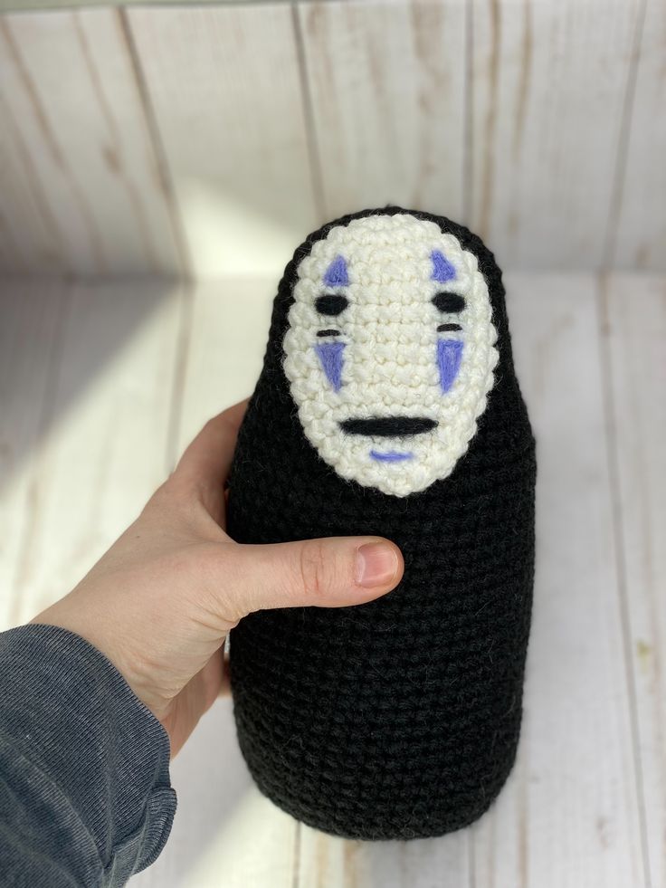 a hand holding a crocheted black and white object with a face on it