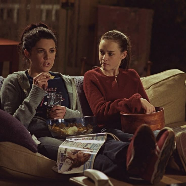 two women sitting on a couch eating and drinking