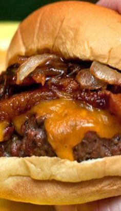 a close up of a person holding a hamburger with cheese and meat on it in their hand