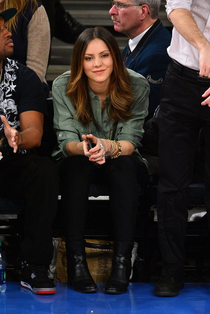 a woman sitting next to a man at a basketball game wearing black pants and green shirt