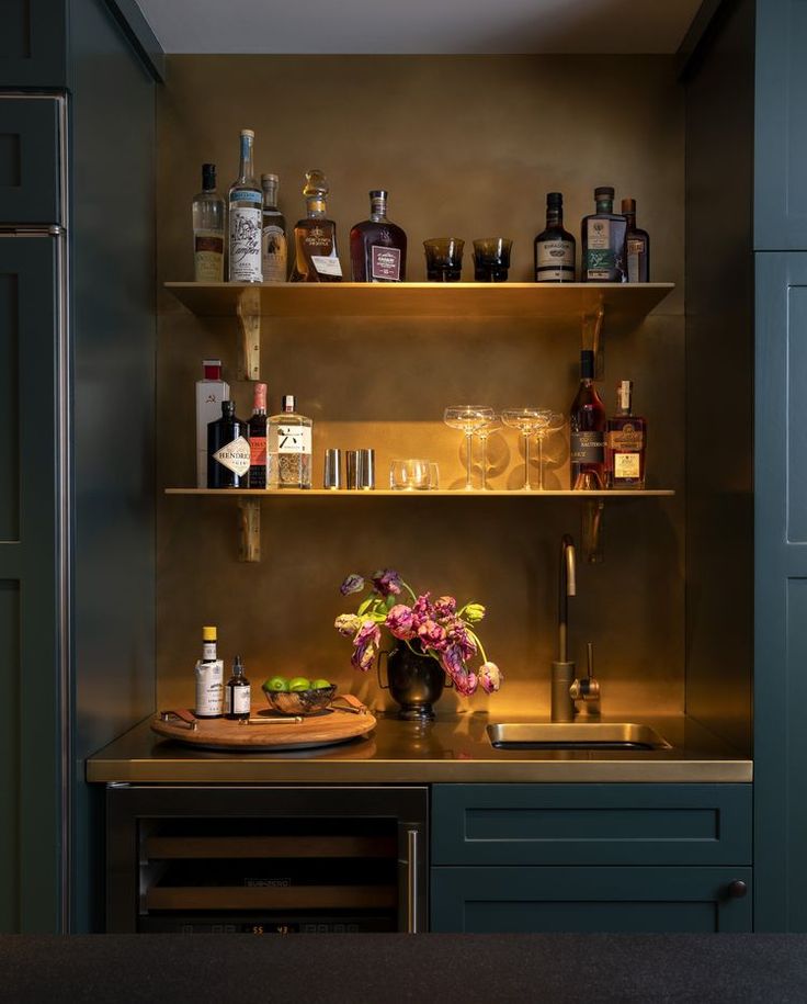 a kitchen with green cabinets and shelves filled with liquor bottles, wine glasses, and flowers