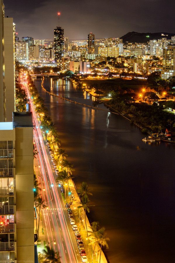 an aerial view of a city at night with the lights streaking across the water