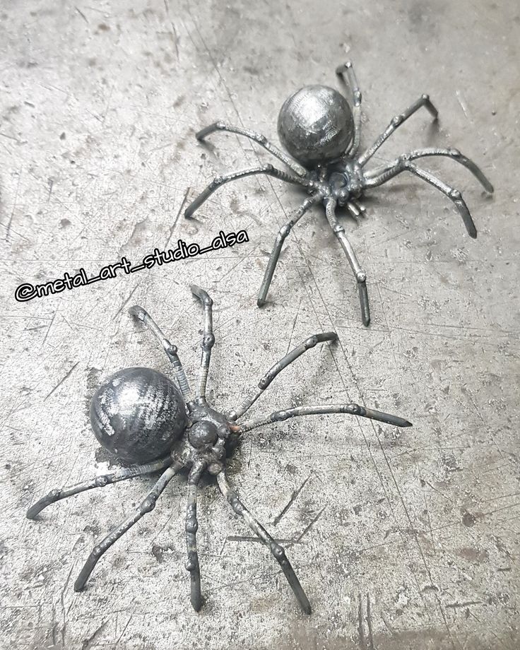 two metal spider sculptures sitting on top of a cement floor