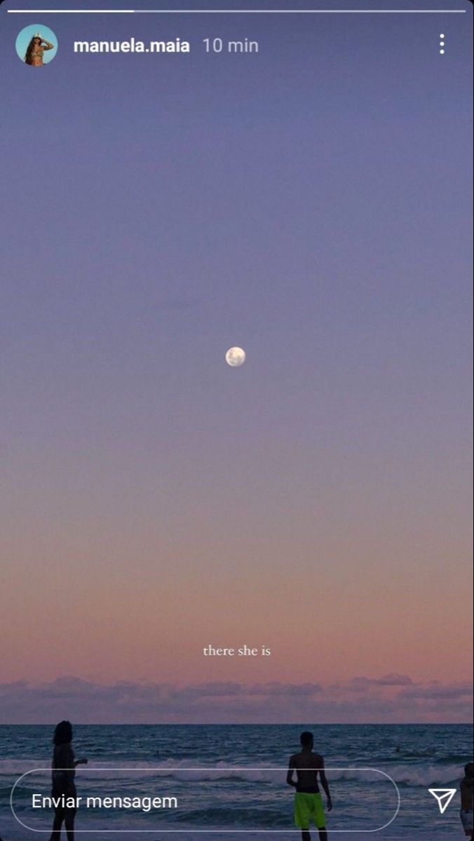 two people are standing on the beach watching the moon rise over the ocean and mountains