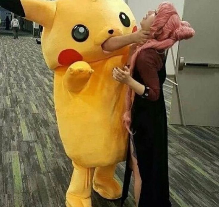 a woman standing next to a giant pikachu mascot in an office building with another person touching it's face