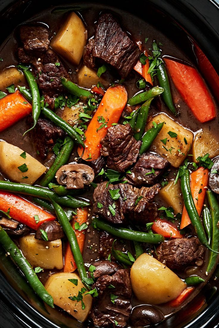 a crock pot filled with beef, carrots and green beans on top of potatoes