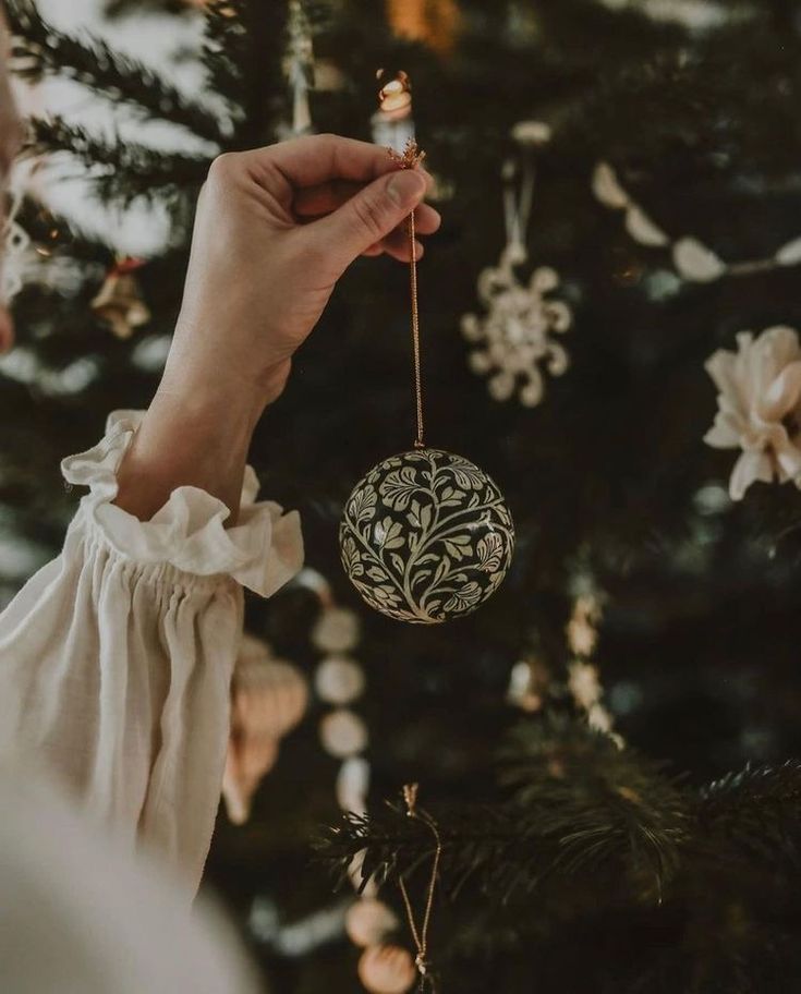 a hand holding an ornament in front of a christmas tree with ornaments on it