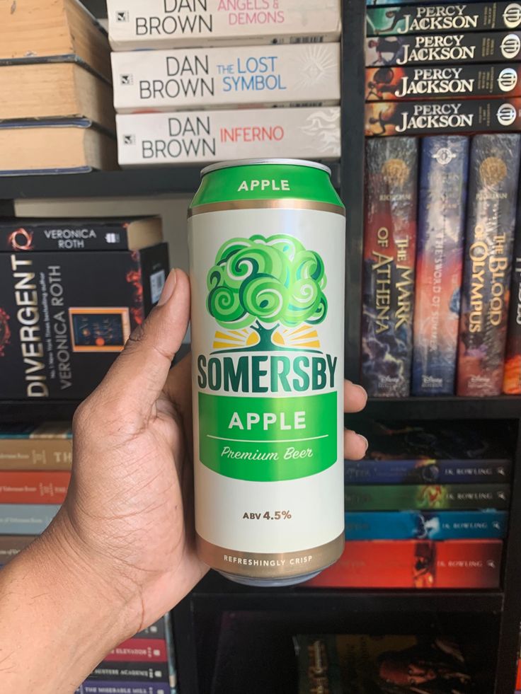 someone holding up a can of somersby apple beer in front of bookshelves