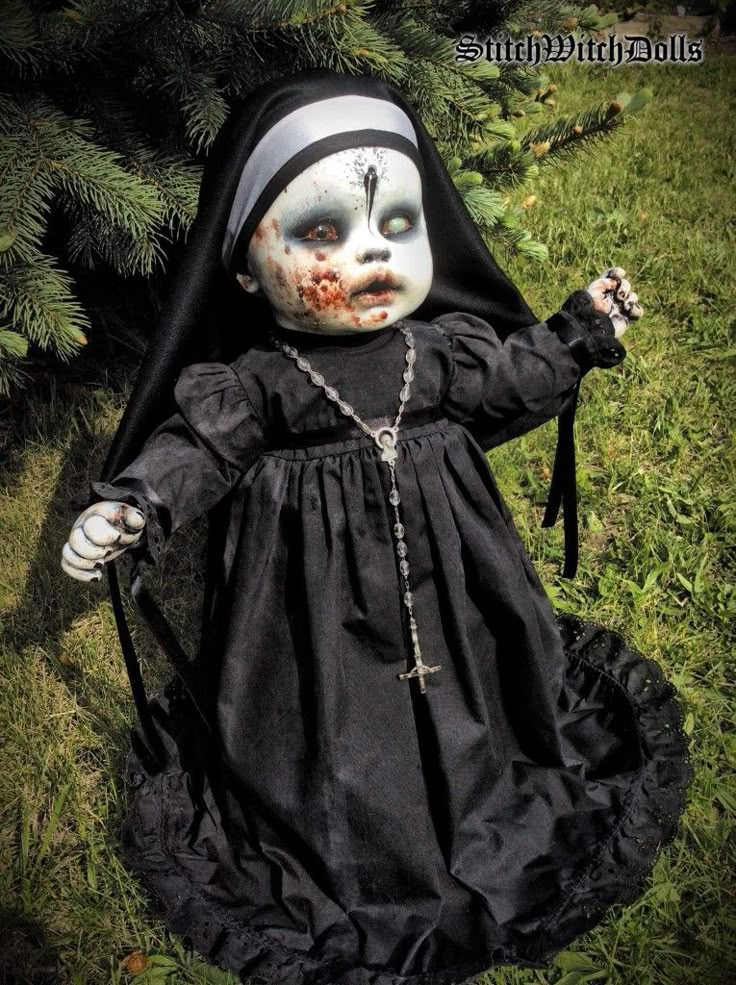 a creepy doll dressed in black with white makeup and blood on her face, sitting in the grass