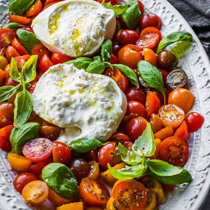 a white plate topped with tomatoes, cheese and green leafy garnishments