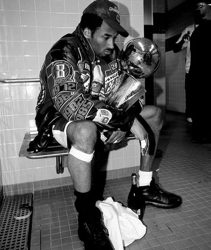 a black and white photo of a man sitting on a bench holding a football helmet