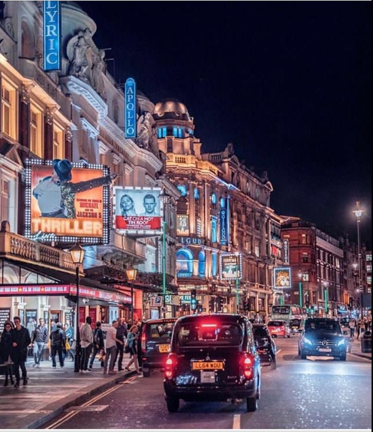 a busy city street at night with people walking and cars driving on the side walk