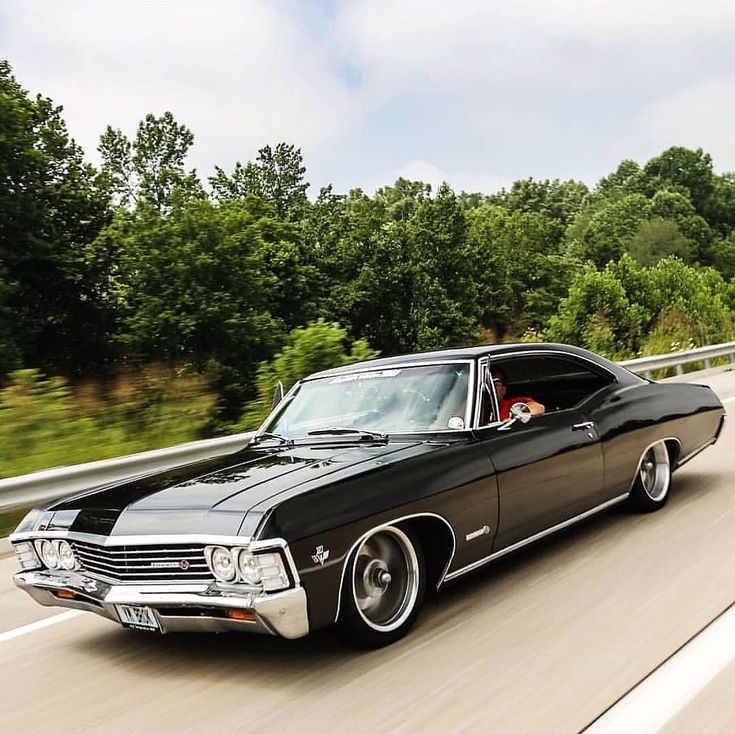 an old black car driving down the road