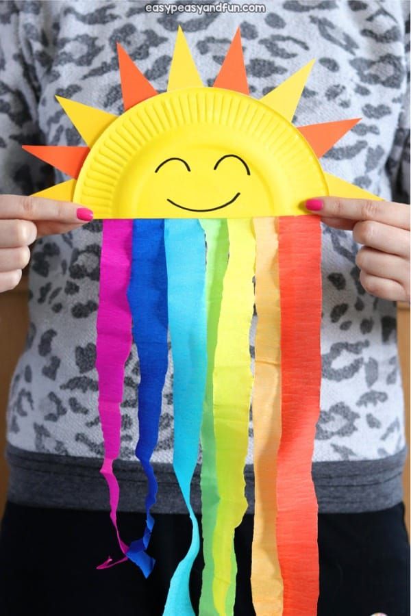 a person holding up a paper plate that has a sun and rainbow streamers on it